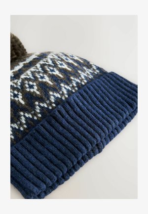 Caciula tricotată cu o margine ribbată de culoare albastru închis. Corpul prezintă un model geometric în nuanțe de maro, alb și albastru, fiind completată cu un pompon maro.