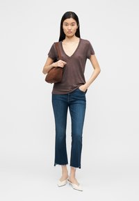 Γυναίκα που φοράει καφέ μπλουζάκι V-neck, κομμένα μπλε τζιν με φθαρμένα τελειώματα, άσπρα τακούνια με μυτερή μύτη και καφέ τσάντα ώμου.