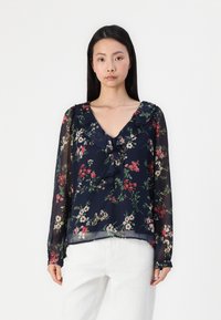 Blouse florale navy avec des manches longues transparentes, un col froncé et des motifs botaniques multicolores en rouge, blanc et vert.