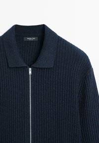 Maglione blu navy a costine con zip e collo, caratterizzato da una zip argentata e dall'etichetta visibile del marchio Massimo Dutti all'interno del collo.