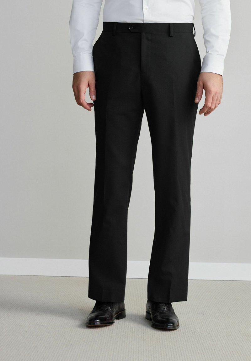 Pantalones de vestir negros con diseño de pierna recta, que presentan una parte delantera plana y trabillas para cinturón. El material parece suave y ligero. Combinados con zapatos negros.