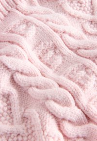 Svetlo rožnata pletena tkanina z teksturiranim vzorcem kabelskega pletenja, z izbočenimi šivi, ki ustvarjajo globino in vizualno zanimivost po celotni površini.