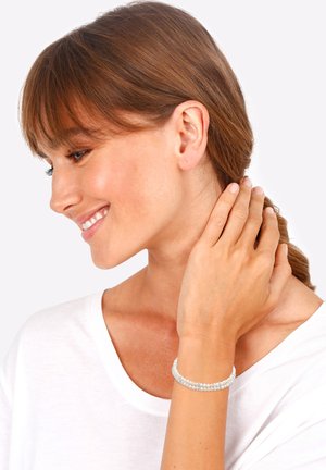 Bracelet en perles avec des perles bleu clair et transparentes, dotée d'une finition lisse et brillante. Porté au poignet, mettant en valeur un design superposé.