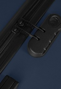 Tiradores dobles de cremallera negra asegurados con un candado de combinación de tres dígitos sobre la superficie texturizada de una maleta azul oscuro.