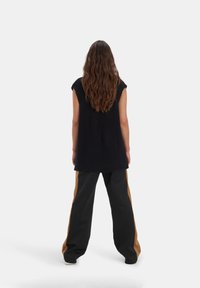 Veste oversize tricotée bleu marine à manches courtes, présentant un motif texturé. Associée à un pantalon noir avec des bandes latérales beige.