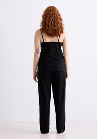 Zwarte mouwloze top en loszittende zwarte broek, gemaakt van zachte stof, met een ontspannen ontwerp met spaghettibandjes en zonder zichtbare patronen.