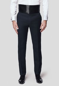 Czarne spodnie z szerokim satynowym paskiem w talii, dopasowany krój i subtelne szczegóły w paski. W połączeniu z błyszczącymi czarnymi butami formalnymi.