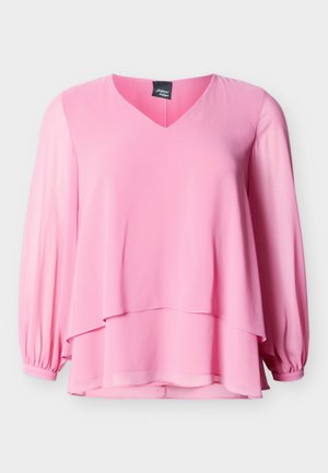 Bluză roz deschis cu mâneci lungi, decolteu în V și tiv stratificat, cu manșete adunate la mâneci, pe un fundal simplu.