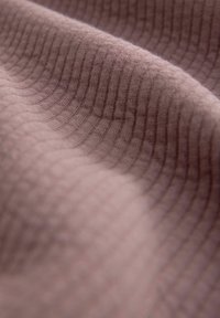 Tejido de color rosa suave, con una textura ribeteada y un suave patrón de ondas a lo largo de su superficie.