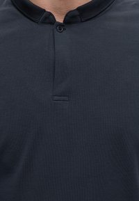 Gros plan d'une personne portant une chemise en coton bleu foncé avec un seul bouton et un col montant.