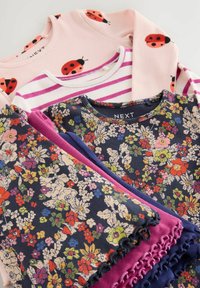 Trois hauts pour enfants à manches longues avec des rayures florales, roses et violettes, ainsi que des motifs de coccinelles roses, empilés et soigneusement pliés.