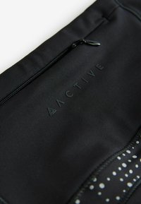 Pochette zippée noire en matériau doux, dotée d'un logo en relief et d'accents à motif de points le long du bord inférieur.