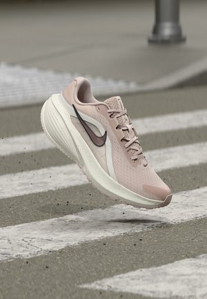 En enkelt lyserød og hvid Nike løbesko med sort swoosh-logo, der svæver over en fodgængerovergang.