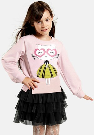 Lichtroze sweatshirt met een katafbeelding die hartvormige brillen draagt, in combinatie met een zwarte gelaagde tule rok en witte met patronen bedrukte panty’s.