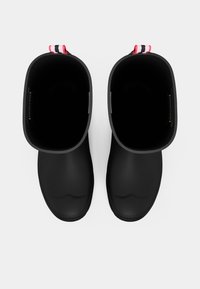 Fekete gumicsizmák széles nyílásokkal, sima felülettel és kontrasztos piros-fehér szövetfülekkel a könnyű felhúzáshoz. Lapostalpú, minimalista dizájn.