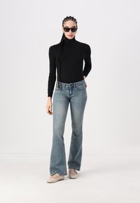 Svart langermet turtleneck skjorte, lyseblå flagrende jeans med en svak falming, og beige leiligheter. Tilbehør inkluderer svarte solbriller.