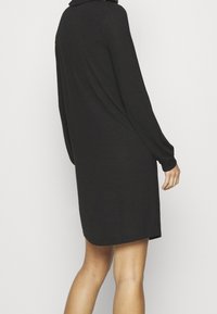 Schwarzes Langarmkleid mit Kragen, aus einem strukturierten Stoff gefertigt, mit einem geraden Schnitt, der über dem Knie endet.
