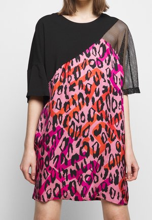 Woman wearing a short dress with black top, pink-red leopard print bottom, and one sleeve made of black mesh fabric.