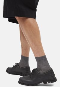 Musta kumisaappaat nauhoilla, joissa on paksut, kuvioidut pohjat ja hienovarainen kaareva muotoilu, käytetään harmaiden nilkkasukkien ja mustien shortsien kanssa.