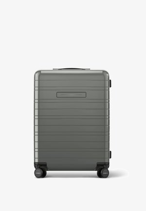 Valise rigide grise avec des lignes verticales, une poignée noire sur le dessus et quatre roues, dotée d'une finition lisse et brillante.