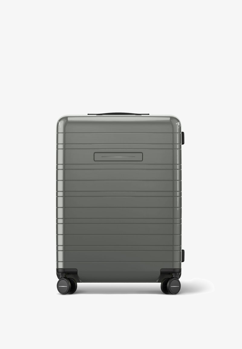 Valise rigide grise avec des lignes verticales, une poignée noire sur le dessus et quatre roues, dotée d'une finition lisse et brillante.