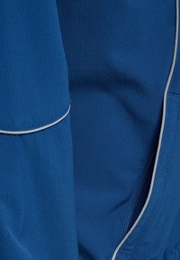 Nahaufnahme eines blauen Stoffes mit strukturiertem Muster und hellgrauem Paspel entlang der Nähte, die die detaillierte Nahtführung und Materialstruktur hervorhebt.