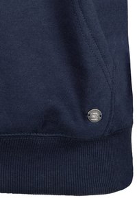 Sudadera de algodón azul marino con dobladillo acanalado, que presenta un acento de logo circular plateado cerca de la parte inferior izquierda, tejido texturizado con costuras visibles.