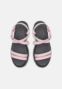 Růžové kožené sandály se dvěma širokými popruhy přes černou pěnovou podešev, zahrnující kotníkový pásek se stříbrnou sponou a embosovaným logem.