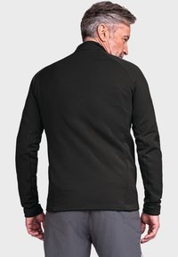 Schwarze, langärmlige Jacke mit glatter Textur, hochgeschlossen und eng geschnitten. Es sind sichtbare Nähte an den Schultern und an den Seiten vorhanden.