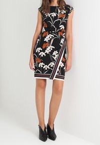 Vestido negro de flores con mangas cortas, que presenta flores blancas y naranjas, un diseño envolvente y un dobladillo a rayas. Combinado con botas negras hasta el tobillo.
