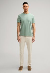 Mintgrünes Baumwoll-T-Shirt mit Rundhalsausschnitt, kombiniert mit hellbeigen Hosen und braunen Slippern. Einfaches, lässiges Outfit.