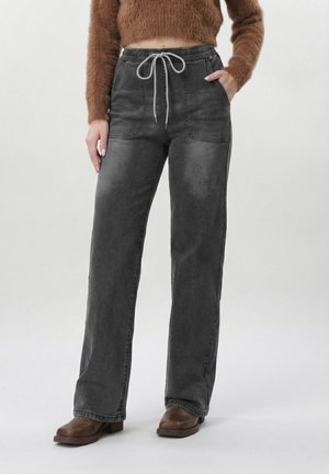 Ținută casual cu pantaloni largi de culoare gri închis, cu talie cu șnur, asortați cu cizme maro și un pulover maro scurt cu textură pufoasă.