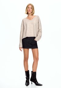 Bež krojeni pulover iz mehke tkanine, v kombinaciji s temno jeans mini krilom. Črne usnjene gležnjarje z zadrgo.