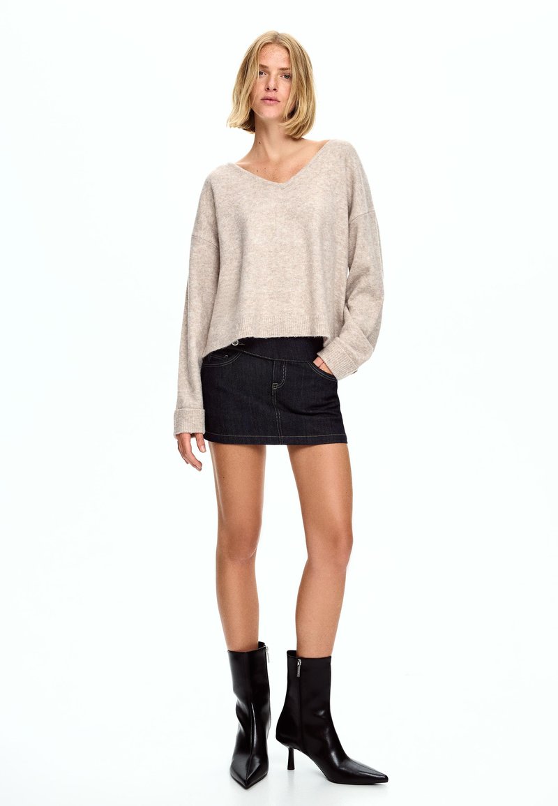 Bež krojeni pulover iz mehke tkanine, v kombinaciji s temno jeans mini krilom. Črne usnjene gležnjarje z zadrgo.
