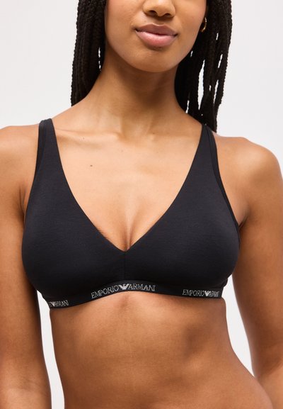 Γυναίκα που φοράει μαύρο τριγωνικό σουτιέν με λεπτούς ιμάντες και ελαστική ταινία Emporio Armani κάτω από το στήθος.
