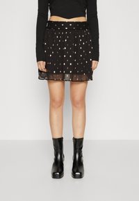 Svart plisserad kjol med metalliska prickmönster, lättvikts, semi-genomskinligt tyg, elastisk midja, tillsammans med svarta ankelkängor.