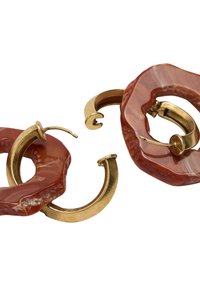 Złote kolczyki w kształcie obręczy z nieregularnymi, masywnymi, czerwonobrązowymi pętlami z żywicy, prezentujące połączenie gładkich i teksturowanych powierzchni na białym tle.
