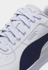 Λευκό δερμάτινο αθλητικό παπούτσι με ναυτικό λωρίδα, λευκά κορδόνια και ανάγλυφο λογότυπο Puma στο πλάι και στη γλώσσα, κοντινή όψη.