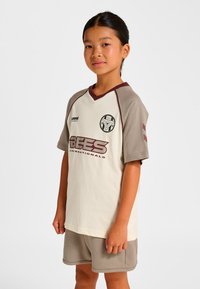 Helles kurzärmeliges Fußballtrikot mit kastanienbraunen Akzenten, "BEES"-Logo und grauen Ärmeln. Kombiniert mit passenden grauen Shorts. Weicher Stoff.