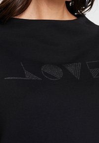 Sweat-shirt noir avec un design texturé "LOVE" en finition brillante, intégrant des formes géométriques dans les lettres. Matériau doux.