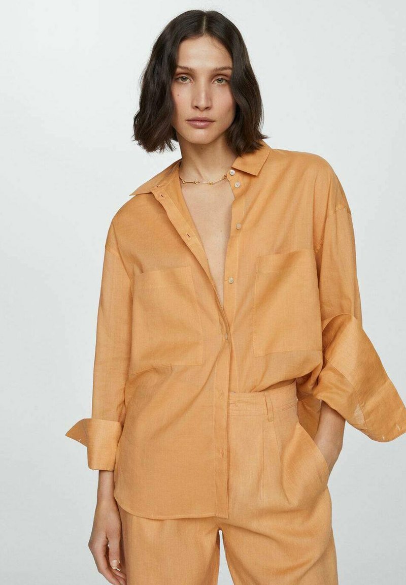 Camicia di lino arancione chiaro con una vestibilità rilassata, chiusura con bottoni, maniche lunghe arrotolate ai polsini e due tasche frontali.