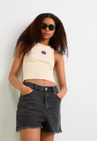 Crème geribbelde crop top met een blauwe "Santa Cruz"-logo, gecombineerd met hooggeprofileerde zwarte denim shorts met rafelige randen.