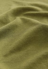 Tissu doux vert olive avec une texture fine en maille et de plis légers créant des ombres et des reflets subtils.