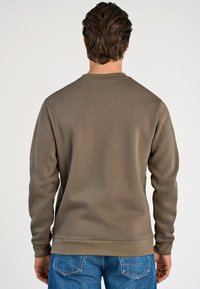 Sudadera marrón, texturizada, de manga larga y cuello redondo, con un dobladillo acanalado. Combinada con jeans de mezclilla azules sobre un fondo neutro.