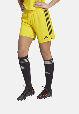 Geel voetbalshorts met zwarte strepen, gecombineerd met zwarte sokken met witte strepen en zilveren accenten, en zwarte voetbalschoenen met rode details.