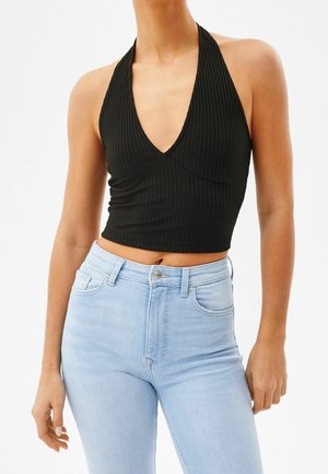 Zwart geribd halter crop top met een diepe V-hals, gecombineerd met lichtblauwe jeans met hoge taille. De stof is rekbaar en heeft een aansluitend ontwerp.