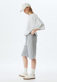 Sudadera de talla grande en gris claro y pantalones cortos a juego, fabricados en una suave tela. Zapatillas blancas con detalles en marrón claro y calcetines color crema. Ajuste casual y relajado.