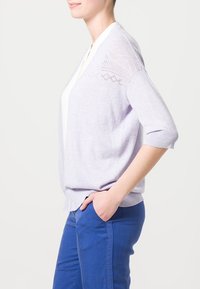 Ljuslila cardigan med lös passform, trekvartsärmar, texturerad spetsdetalj på axlarna, kombinerad med blå byxor.