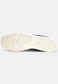 Svart skosula med en texturerad, off-white gummibasin med hexagonalt mönster och spår för grepp.