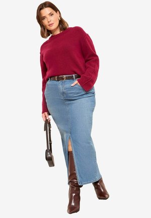 Bordó pulóver hosszú ujjakkal, kék farmer szoknya elülső hasítékkal, barna öv és fényes barna térdig érő csizma.